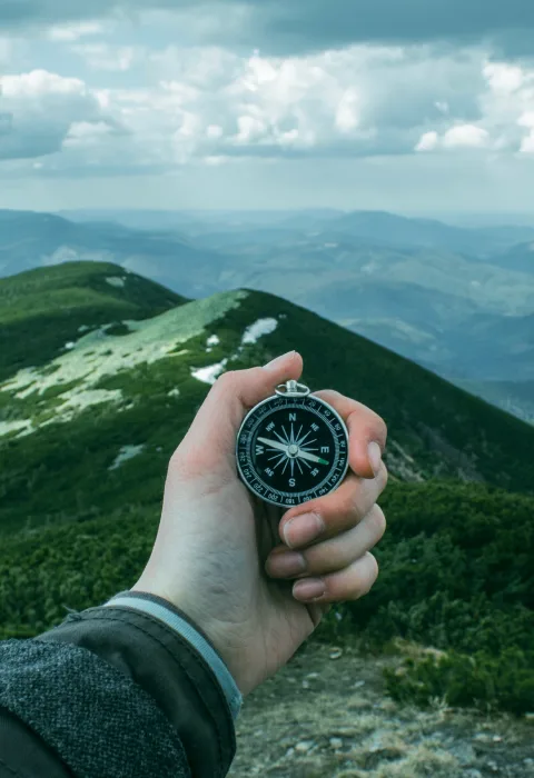 Hand hält einen Kompass vor einer weiten, bewaldeten Berglandschaft